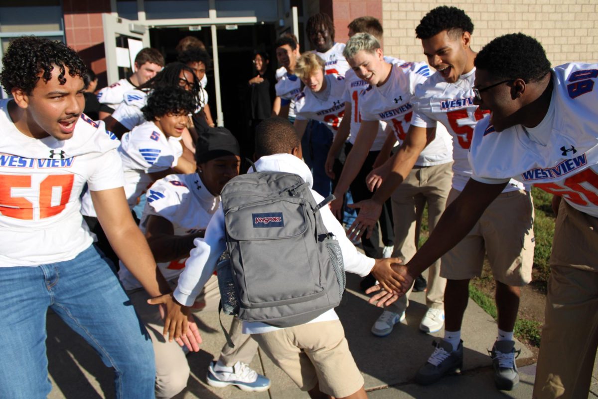A Prairie Wind student runs through the lines of Westview Varsity football players and accepts high fives. The players cheered him on and hyped him up.  